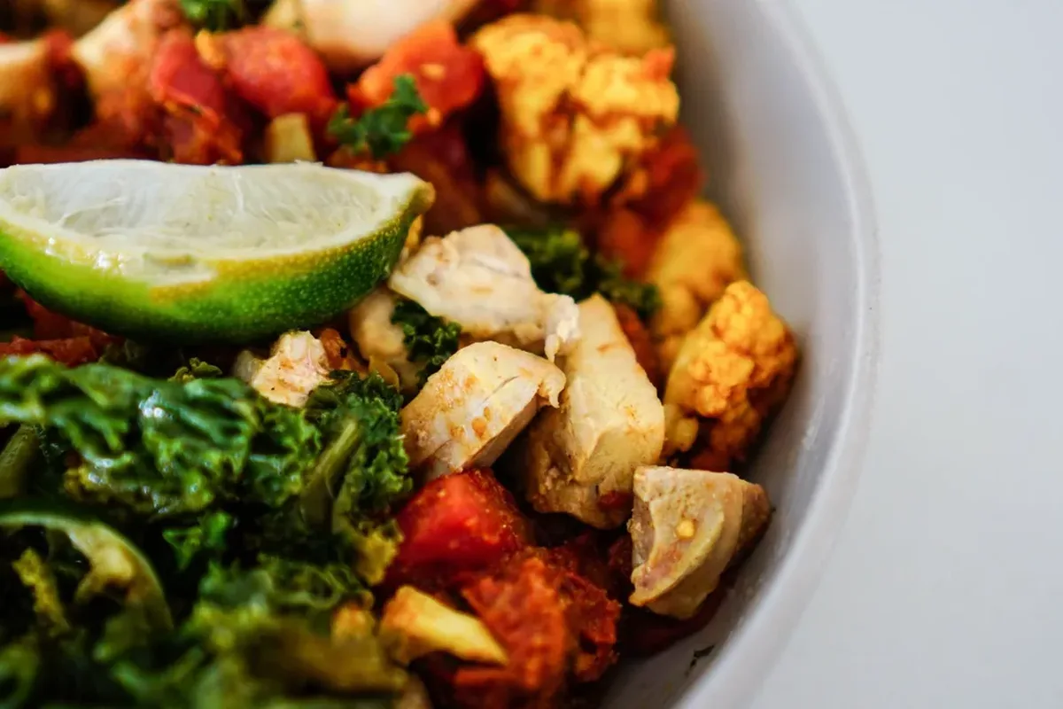 Bowl of chicken salad with kale, shredded vegetables and a lime wedge